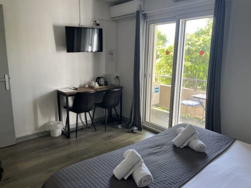 Comfortable hotel room at Hôtel l'Orangeraie Lavandou with bed, desk, TV, and garden view from balcony doors