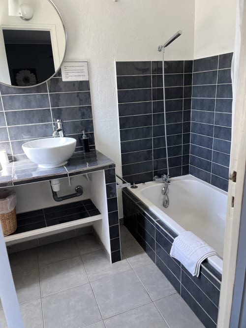 Modern bathroom at Hôtel l'Orangeraie Lavandou with black tiled walls, white vessel sink, bathtub with shower, and round