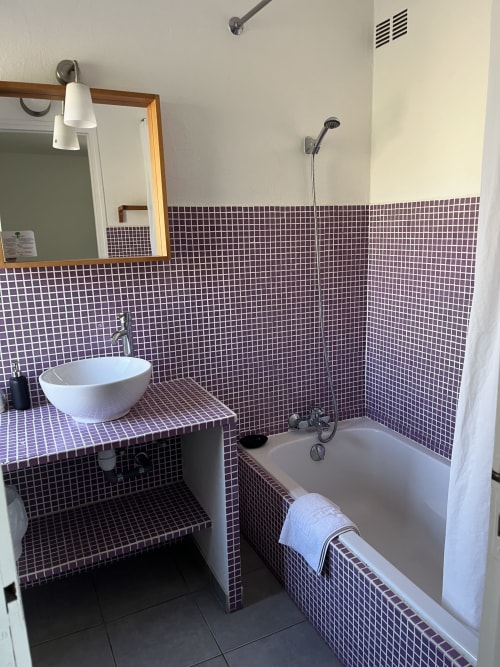 Bathroom in Chambre Confort at Hôtel l'Orangeraie Lavandou with purple mosaic tiling, white vessel sink, bathtub, and shower