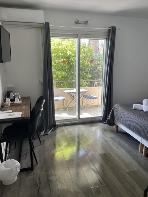 Comfortable hotel room at Hôtel l'Orangeraie Lavandou with garden view, bed, desk, and patio doors overlooking greenery and