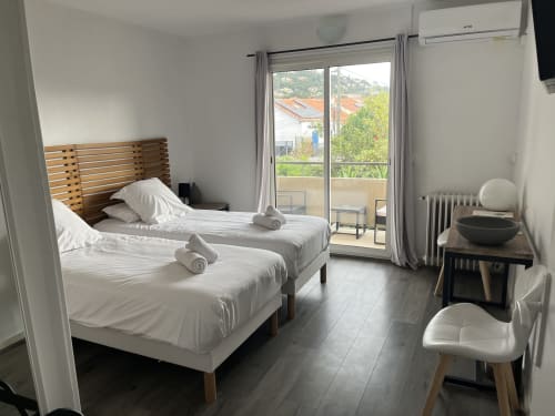 Twin bedroom with garden view, white linens, wooden headboard, air conditioning, and balcony access at Hôtel l'Orangeraie