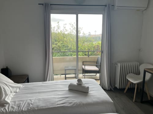 Bright bedroom with white bed, balcony overlooking garden, modern furnishings at Hôtel l'Orangeraie Lavandou
