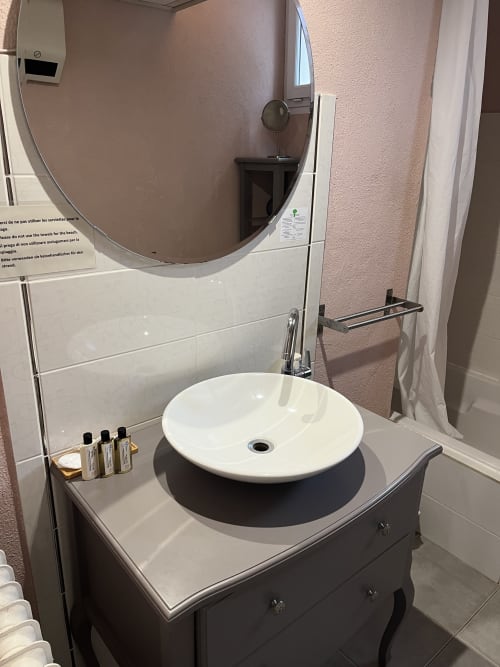 Modern bathroom vanity with white round sink, dark cabinet, and large circular mirror at Hôtel l'Orangeraie Lavandou