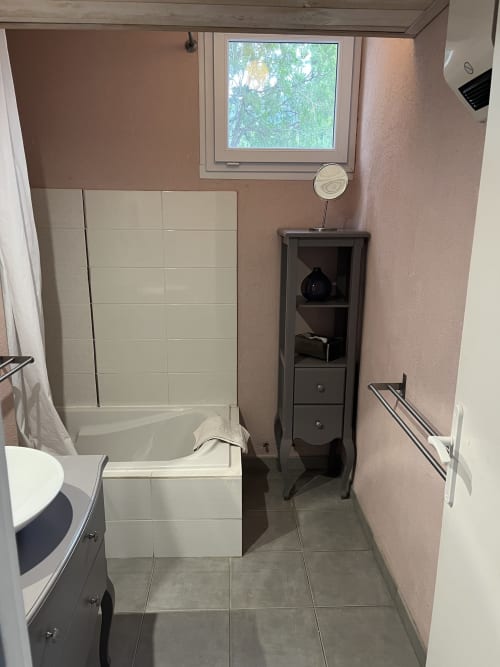 Bathroom with white subway tile surround, bathtub, pedestal sink, dark wooden cabinet, and garden view window at Hôtel
