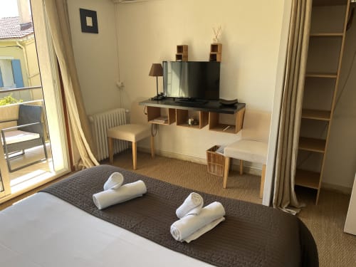 Modern hotel room at Hôtel l'Orangeraie Lavandou with bed, TV, desk, and garden view from balcony