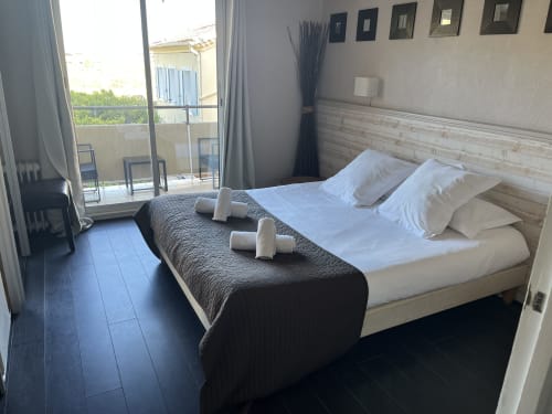 Modern hotel bedroom at Hôtel l'Orangeraie Lavandou with queen bed, garden view balcony, and dark wood floors