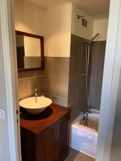 Modern bathroom at Hôtel l'Orangeraie Lavandou with round white sink, wooden vanity, tiled shower, and mirror