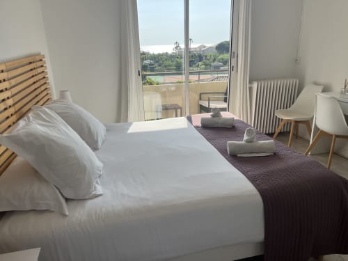 Modern hotel bedroom at Hôtel l'Orangeraie with sea view, wooden bed frame, white linens, and balcony overlooking Le Lavandou