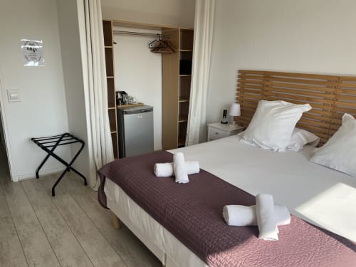 Modern hotel bedroom at Hôtel l'Orangeraie Lavandou with wooden bed frame, white pillows, and rolled towels