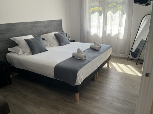 Modern bedroom at Hôtel l'Orangeraie Lavandou with queen bed, dark headboard, white bedding, rolled towels, and glass doors