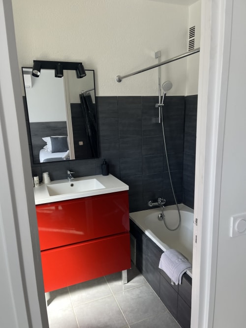 Modern bathroom at Hôtel l'Orangeraie Lavandou with red vanity, black tile walls, and shower setup