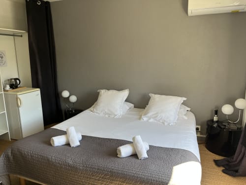 Modern hotel room at Hôtel l'Orangeraie Lavandou with queen bed, white pillows, rolled towels, nightstands with lamps, and