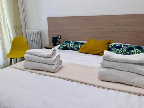 Camera doppia del Costabella Guest House con asciugamani piegati sul letto, sedia gialla, cuscini tropicali e arredi moderni