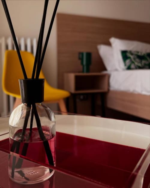 Diffusore rosso su scrivania nella camera doppia della Costabella Guest House con letto e sedia gialla sullo sfondo