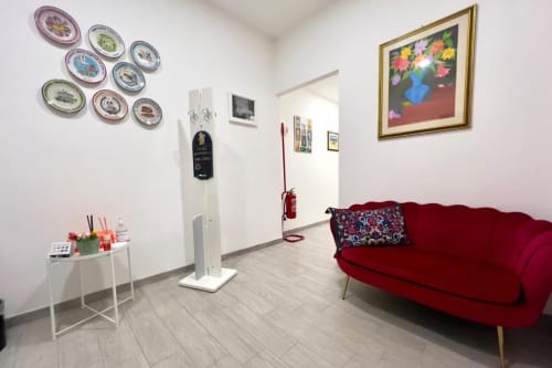 Costabella Guest House Vaticano Prati: luminosa zona comune con divano rosso, piatti decorativi, quadri floreali e camino