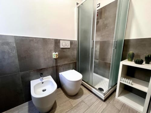 Bagno moderno nella Guest House Costabella con bidet e wc bianchi, pareti in piastrelle scure, cabina doccia in vetro e finiture bianche