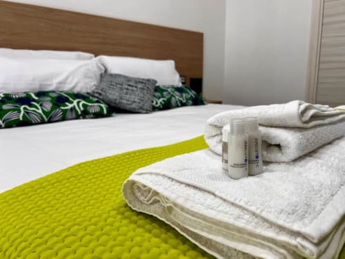 Camera doppia Costabella Guest House con asciugamani bianchi, articoli da toilette e coperta gialla brillante vicino alla testiera in legno