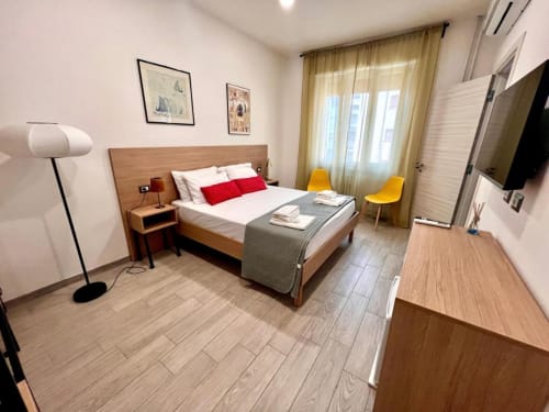 Camera moderna presso Costabella Guest House a Vaticano Prati con letto in legno, cuscini rossi, sedie gialle e vista sulla città