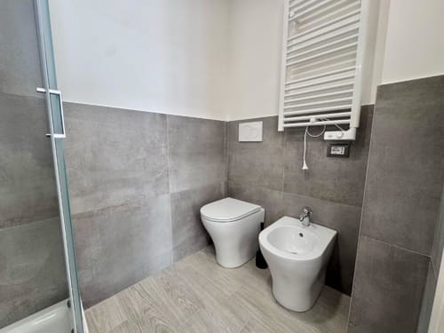 Bagno moderno della Costabella Guest House con wc, bidet, pareti in piastrelle grigie e pavimento in legno chiaro