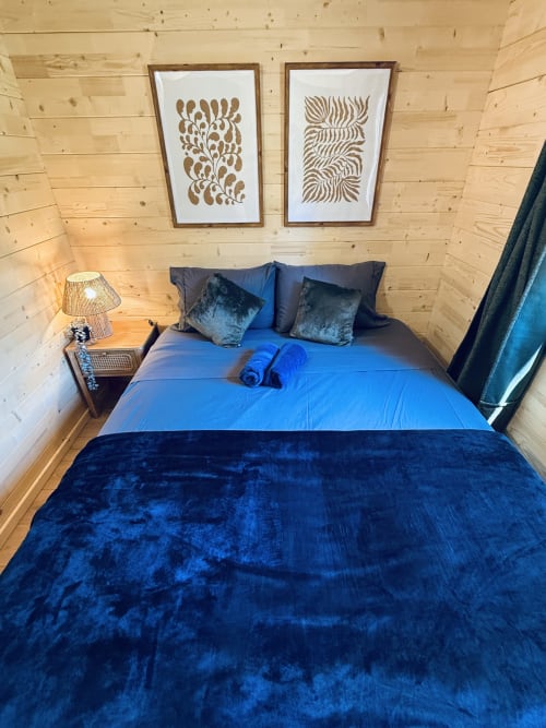 Cozy lodge bedroom with blue velvet bedding, wooden walls, and abstract art at Cabanes et lodges du Belvédère