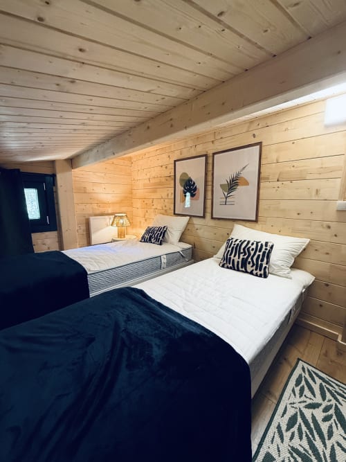 Modern wooden lodge bedroom with two beds, black and white accents, botanical wall art, and warm lighting at Cabanes du