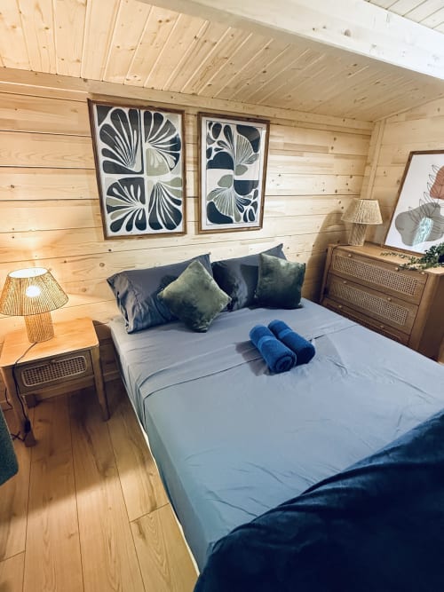 Cozy wooden lodge bedroom with lake views, blue bedding, botanical wall art, and rustic furnishings at Cabanes du Belvédère
