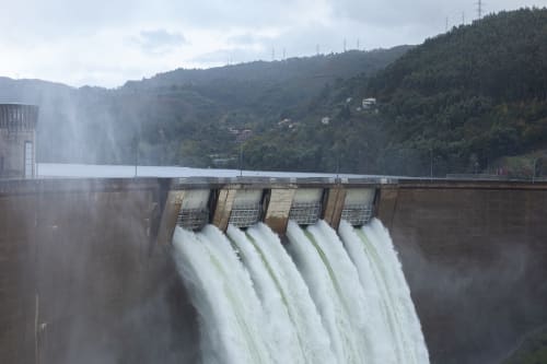 Grande barragem hidrelétrica com poderosos cascatas fluindo através de comportas, cercada por morros florestados em Portugal