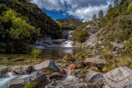 Rio rochoso com água em cascata cercado por vegetação exuberante e paisagem montanhosa em um retiro rural português