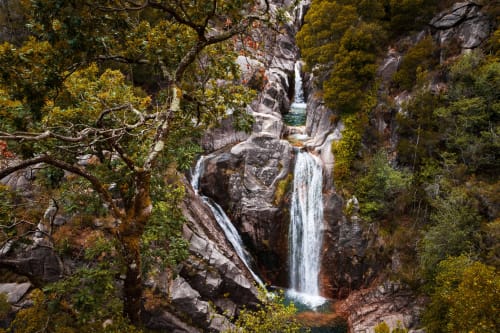 Cachoeira em cascata cercada por vegetação exuberante e rochas cobertas de musgo na Villas Eden, retiro rural em Portugal