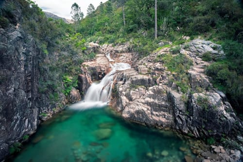 Cachoeira em cascata caindo em piscina esmeralda cercada por penhascos rochosos e vegetação exuberante no retiro rural Villas Eden em Portugal