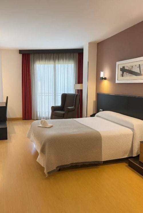 Spacious Deluxe Room at Hotel Villa de Cacabelos with queen bed, balcony, brown accent walls, and modern furnishings