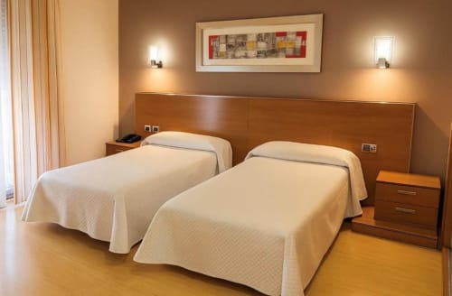 Habitación doble en Hotel Villa de Cacabelos con dos camas individuales, cabecero de madera, pisos de parqué y comodidades modernas