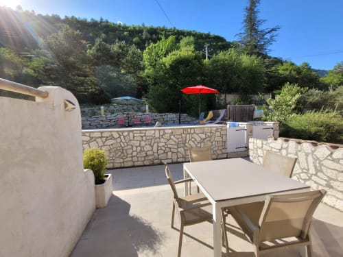 Terrasse avec table à manger et parasol rouge donnant sur la piscine et les jardins du Domaine de la Méouge