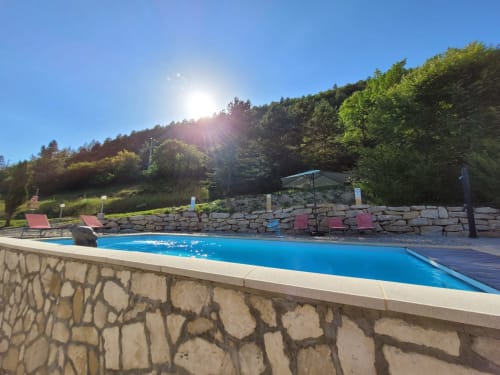 Piscine de villégiature avec chaises longues, parasol et mur de soutènement en pierre au Domaine de la Méouge, campagne française.