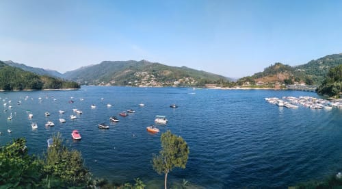 Vista panorâmica de um lago com barcos atracados, montanhas arborizadas e aldeia costeira em Portugal