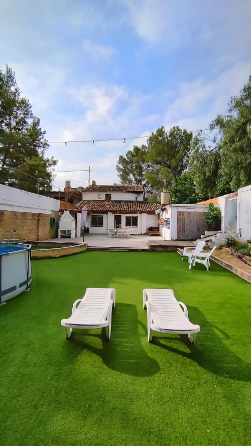 Patio trasero de La Caseta de Ròtova con tumbonas blancas sobre césped artificial y piscina