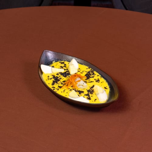 Plato elegante con salsa amarilla, elementos blancos y guarnición negra del restaurante Hotel Balcón De Los Montés en Colmenar