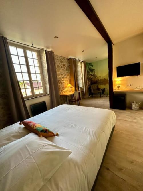 Spacieuse chambre double au Château de la Borde, Ussel, avec lit blanc, grandes fenêtres, poutre en bois foncé et équipements modernes