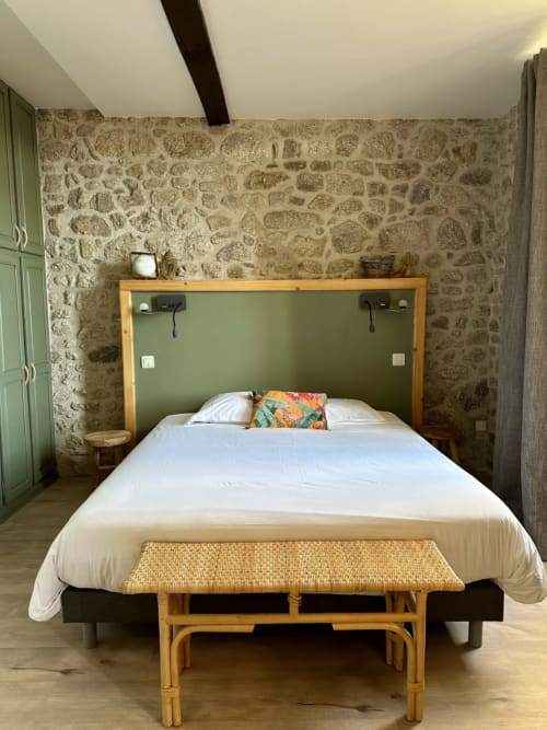 Spacieuse chambre double au Château de la Borde avec murs en pierre, tête de lit verte, banc en bois et literie blanche à Ussel