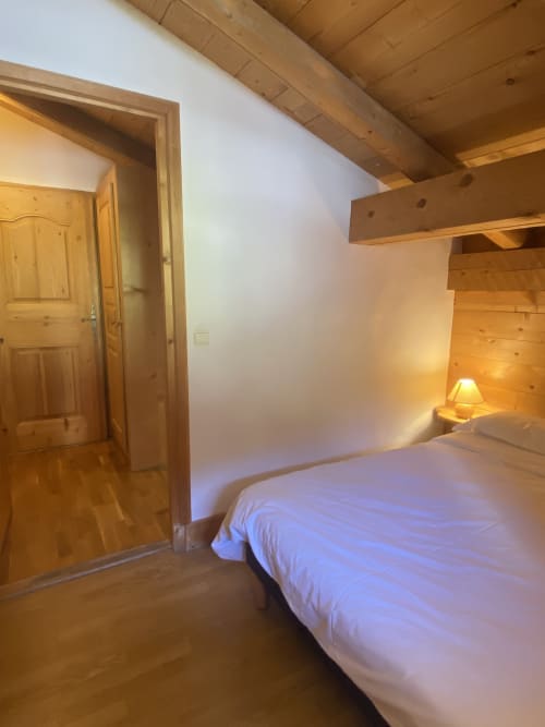 Chambre cosy en bois à La Ferme des Georgières avec lit, lampe de chevet, poutres apparentes et porte en bois