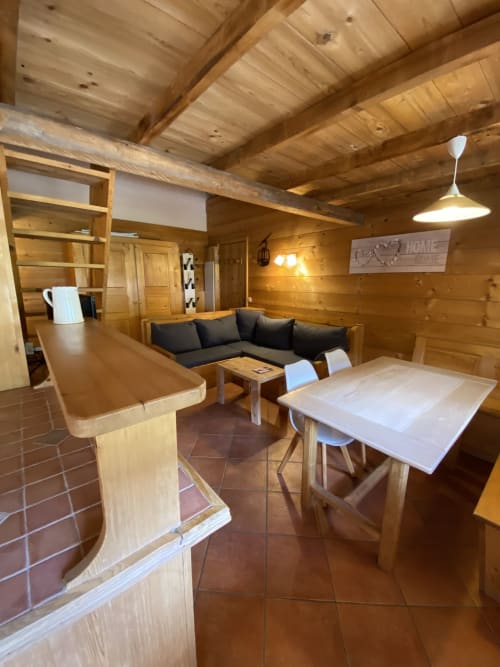 Intérieur de chalet en bois avec table à manger, canapé noir et bar à La Ferme des Georgières, Notre-Dame-de-Bellecombe