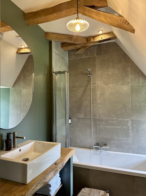 Salle de bain moderne du Manoir du Rigouneix avec lavabo blanc, baignoire, douche à l'italienne et poutres en bois rustique