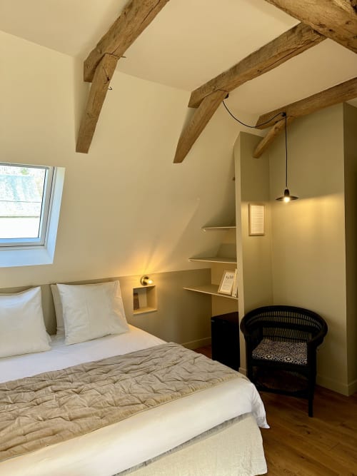 Chambre cosy sous les combles au Manoir du Rigouneix avec poutres apparentes, literie blanche et vue sur le jardin