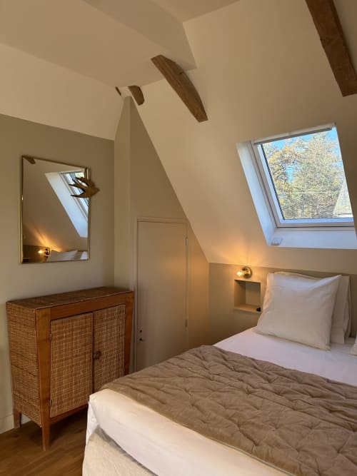 Chambre mansardée moderne au Manoir du Rigouneix avec puits de lumière, poutres apparentes, commode en rotin et vue sur le jardin