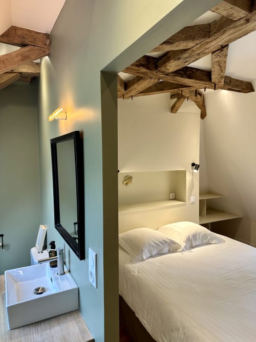Chambre moderne au Manoir du Rigouneix avec poutres apparentes, literie blanche, lavabo attenant et éclairage d'ambiance