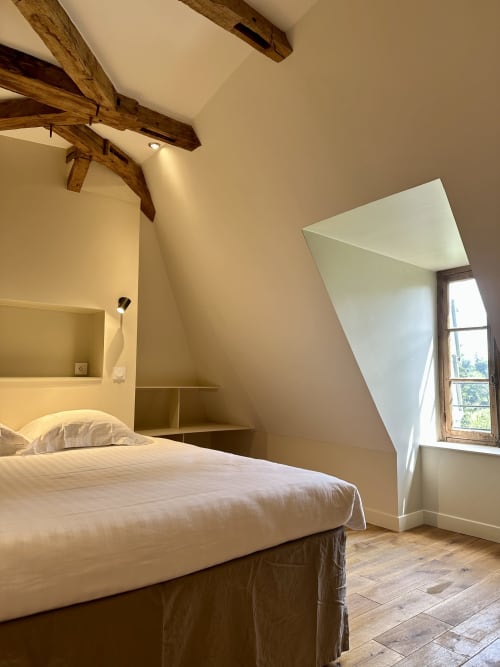 Chambre rustique en mansarde au Manoir du Rigouneix avec poutres apparentes, lucarne et literie crème à Saint-Angel