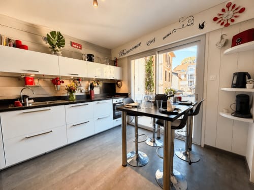 Cuisine blanche contemporaine avec plan de travail noir, table à manger et portes vitrées sur la vue d'Aix-les-Bains 4 étoiles