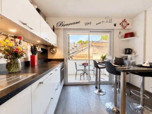 Cuisine moderne avec plan de travail noir dans l'appartement Le 9 Victor Hugo à Aix-les-Bains, ouvrant sur terrasse avec vue sur la ville