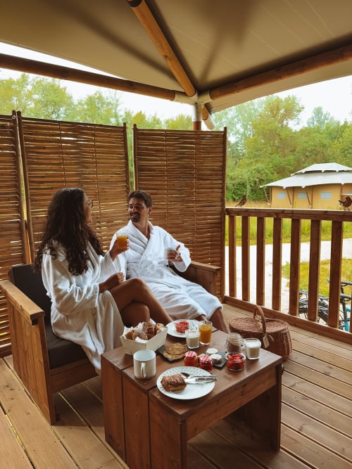 Couple enjoying breakfast on a covered glamping deck at You & Me Glamping in Moncontour, France