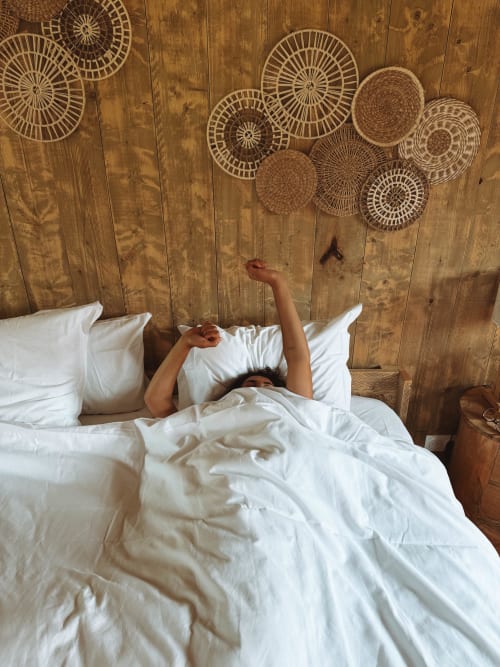Woman stretching in bed at You & Me Glamping, Moncontour, with woven basket wall decor